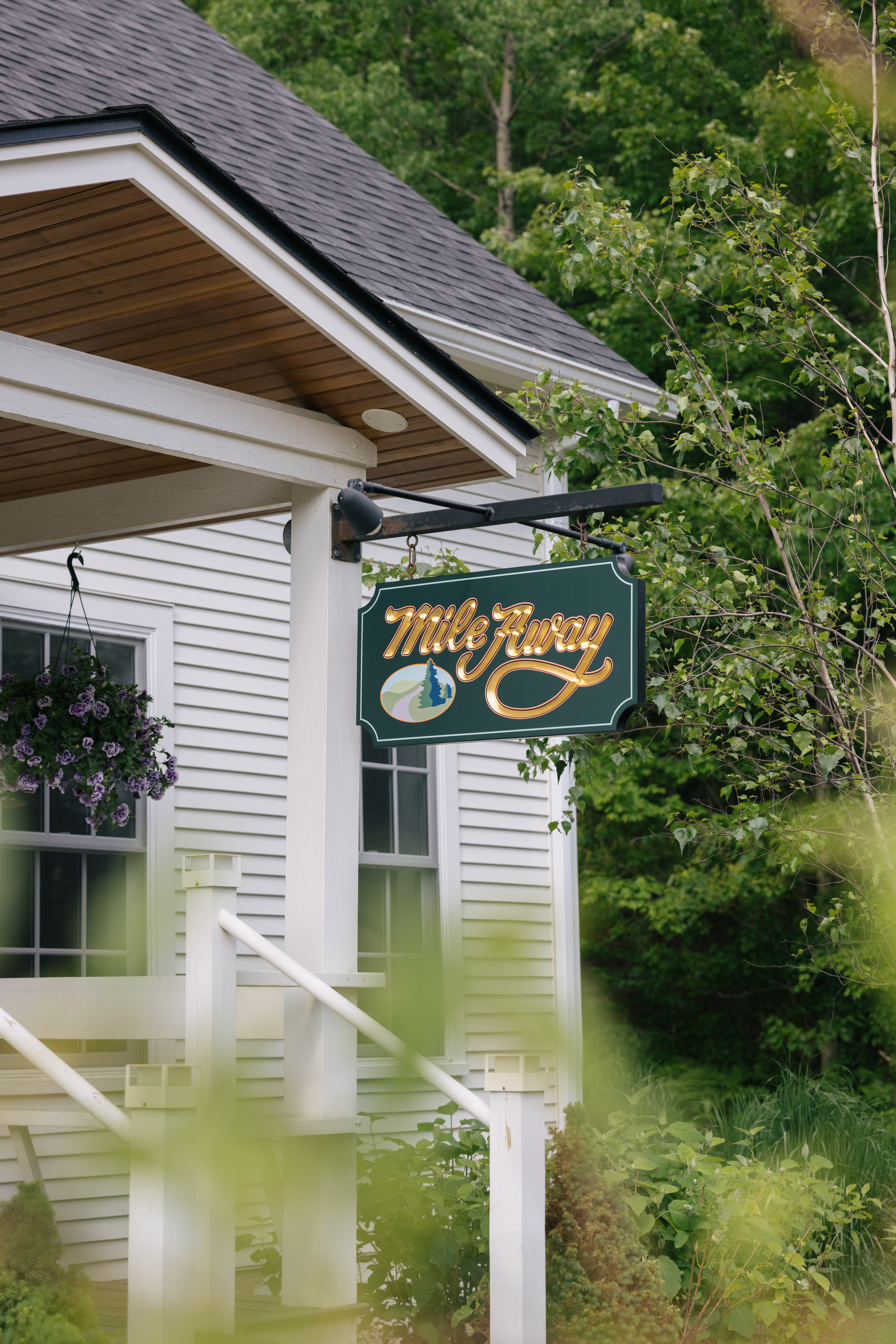 Hanging Mile Away sign on the front porch of the farmhouse surrounded by greenery